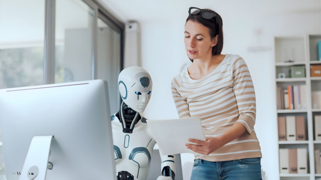 A woman and a humanoid AI robot collaborating on work tasks in a professional office environment.